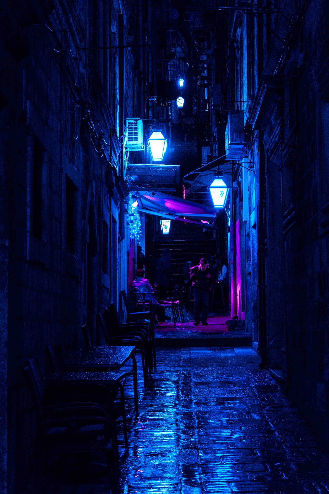 A dark alleyway with a man in the back under pink lights.