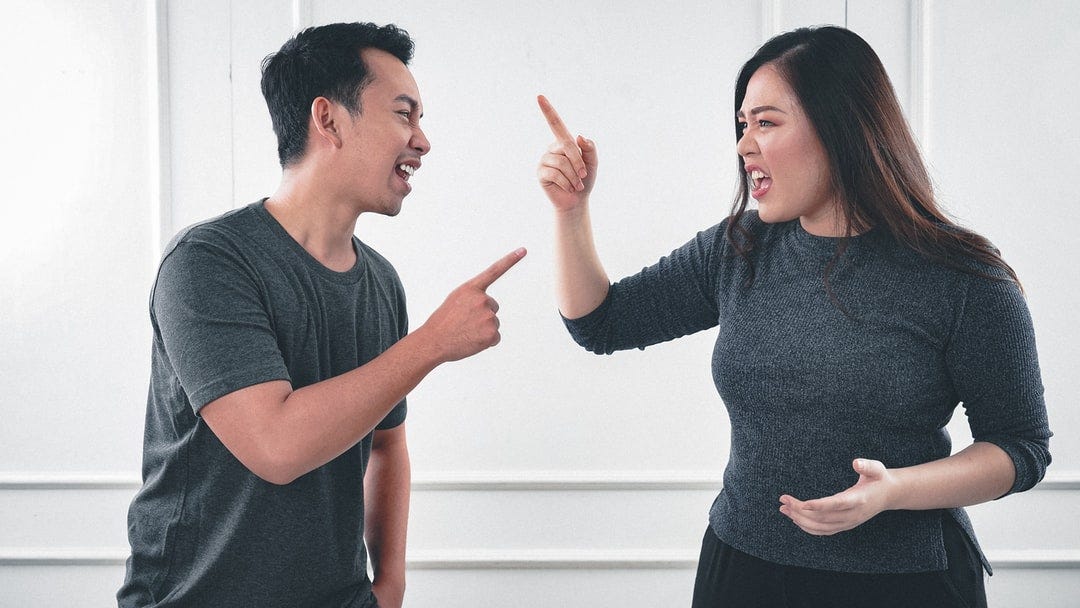 A man and a woman pointing at each other and arguing.