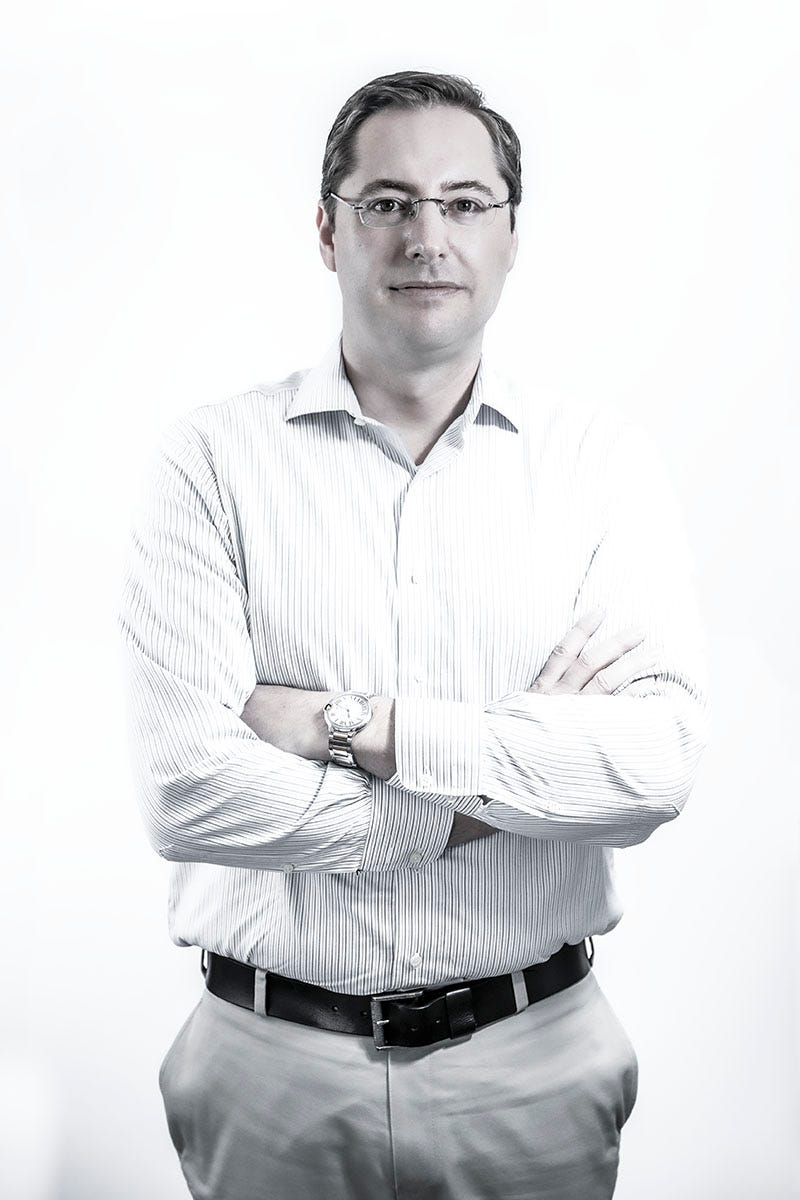 A man in business standing in front of a white background with his arms crossed.