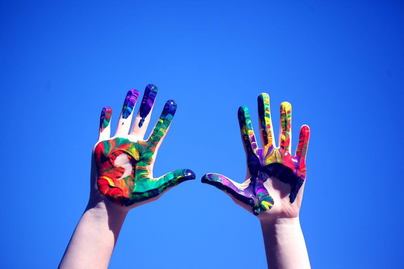 Painty hands held up against a blue sky