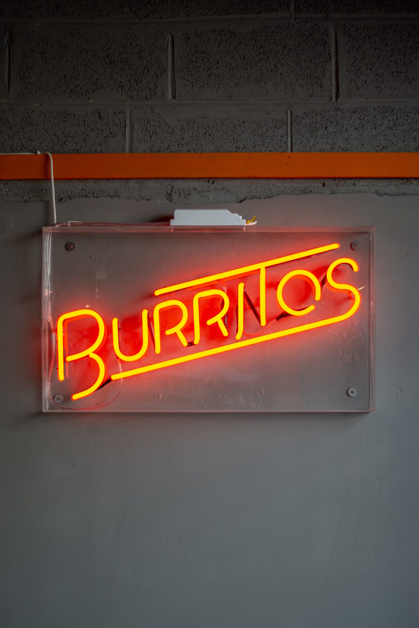 Red neon sign that reads “burritos” against a concrete wall.