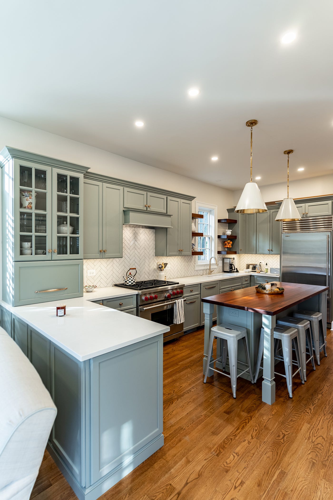 Kitchen with pale green cabinetry, marble white counter tops, and a center island with seating