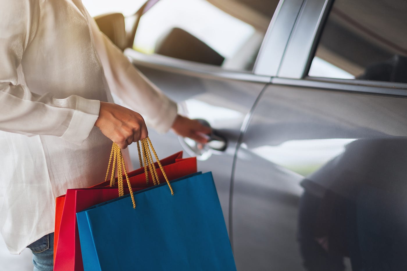 Woman with shopping bags in one hand getting into a car.