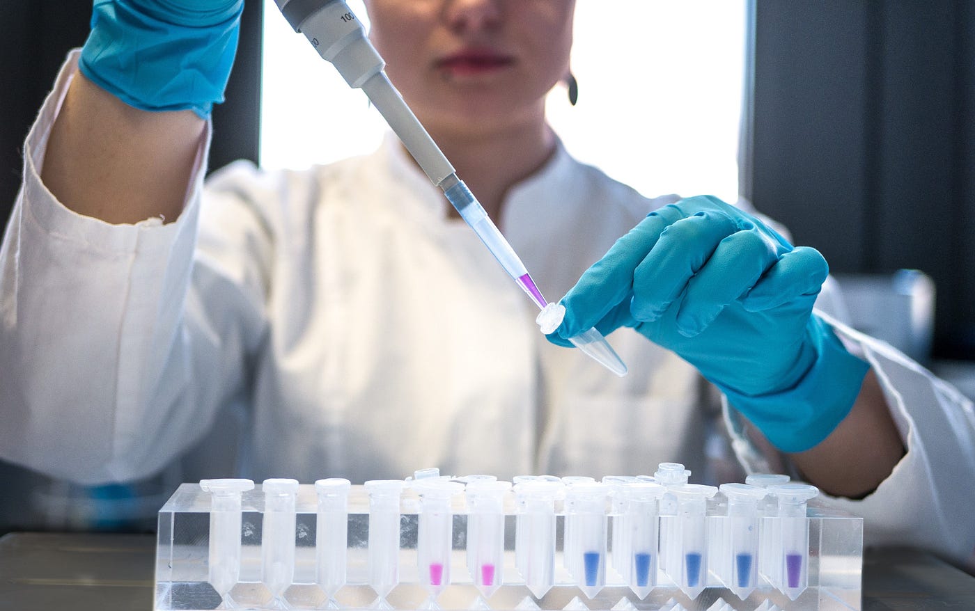 Imagen estándar de una mujer con una bata de laboratorio pipeteando una sustancia coloreada en viales