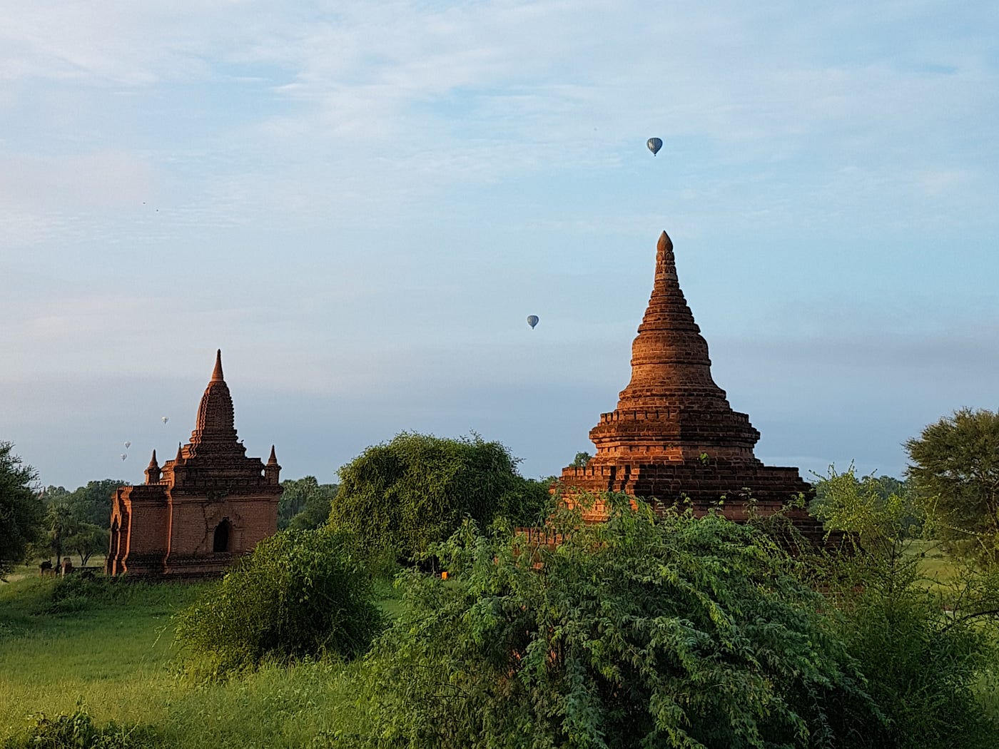 Photo of temple structures in Bagan with hot air balloons in the background