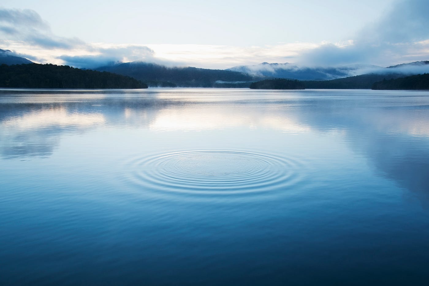 A singular circular pattern ripples on a calm lake’s surface.