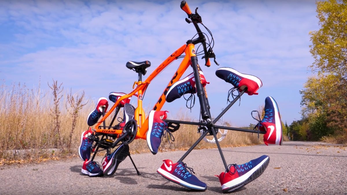 Bicycle whose wheels have been replaced by a dozen running shoes