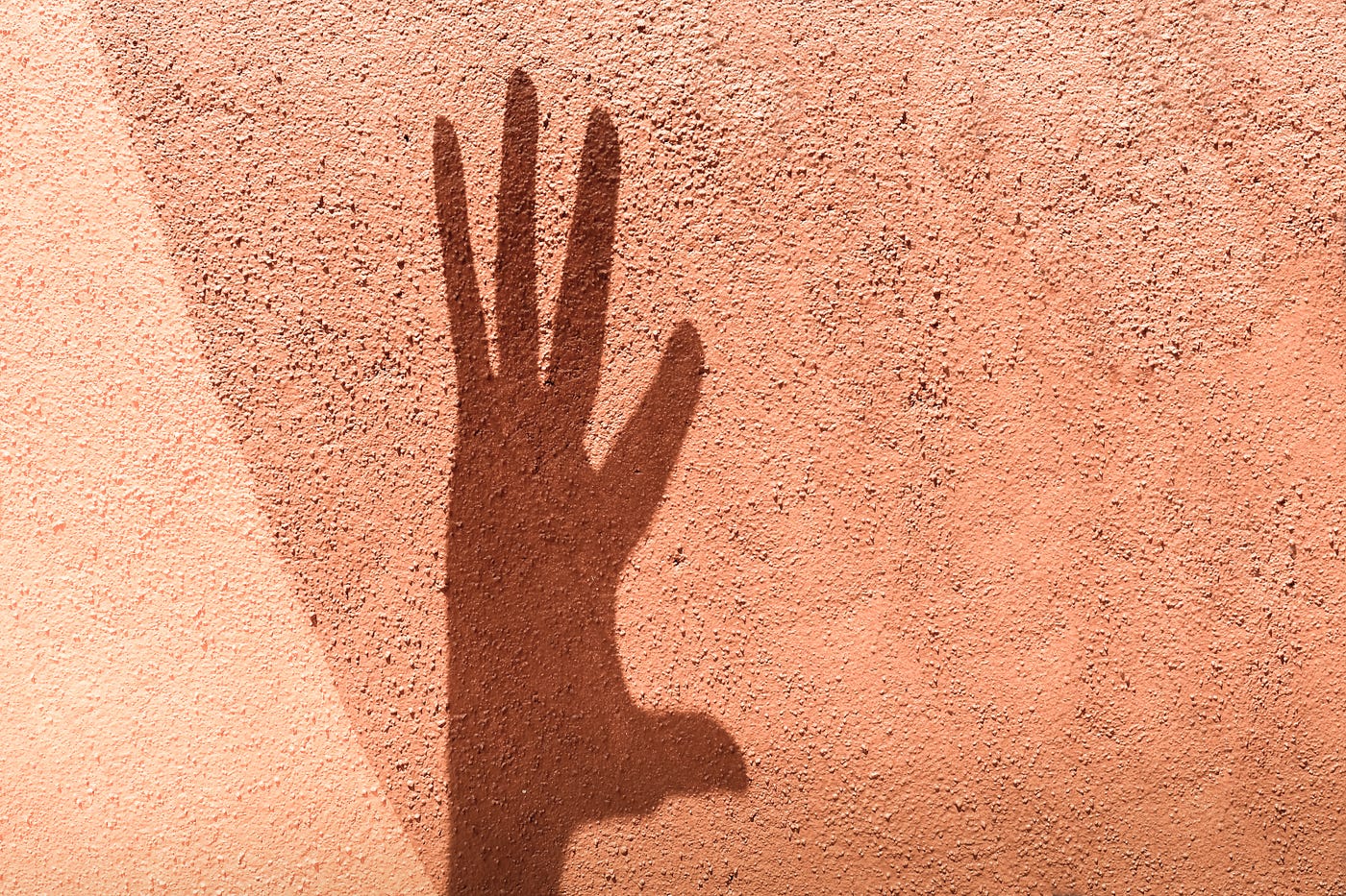 A photo of a shadow of a hand against a peach wall.