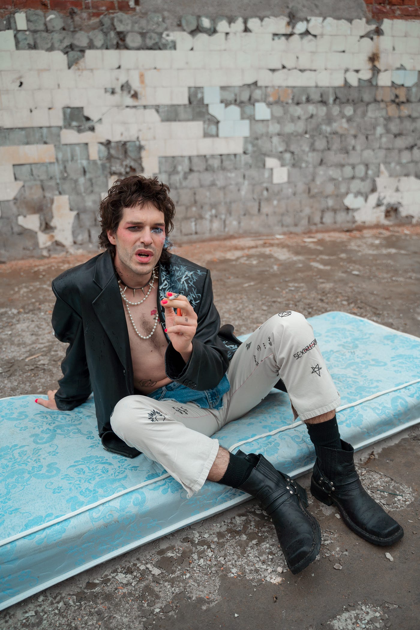 a surly man is dressed as a punk type sitting on an old mattress