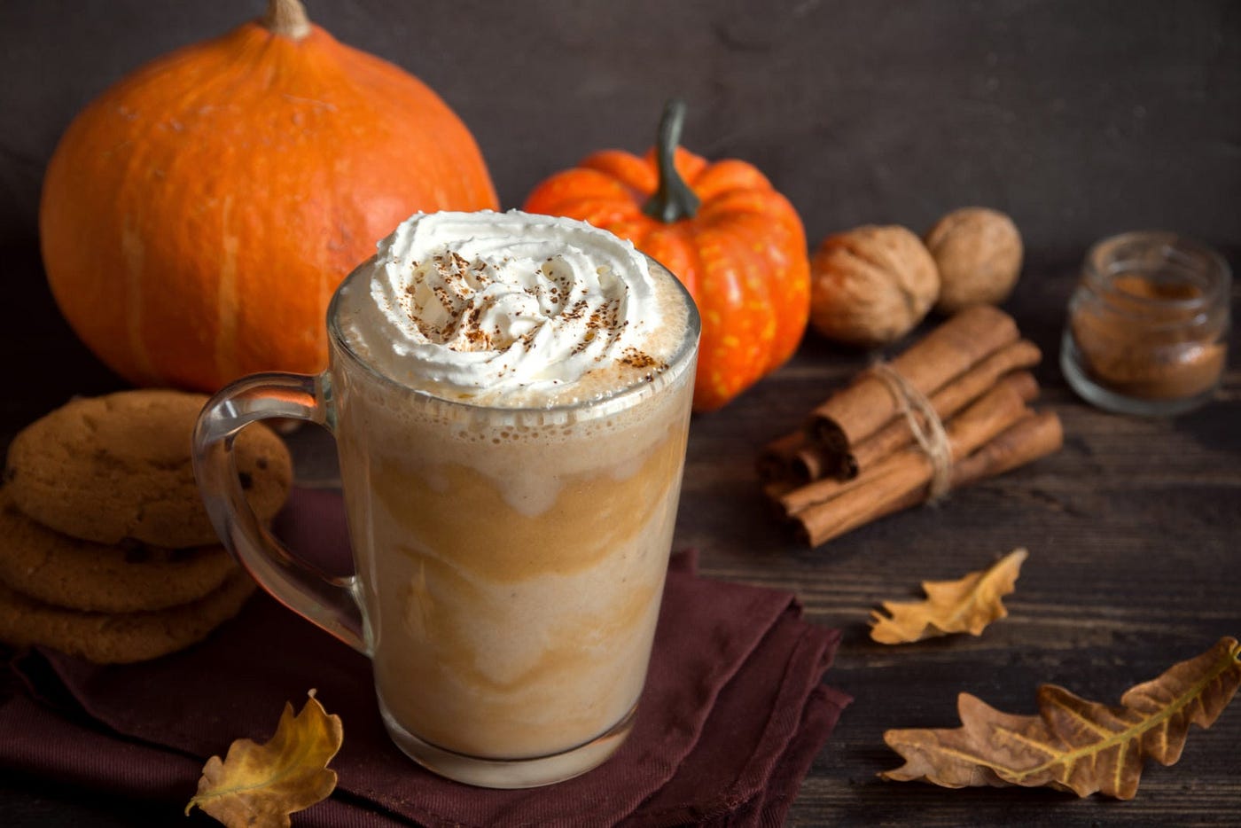 An image of a pumpkin spice latte next to pumpkins, gourds, and cinnamon sticks
