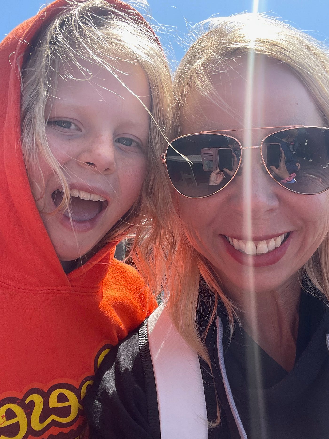 Mother in sunglasses and daughter in orange hoodie.