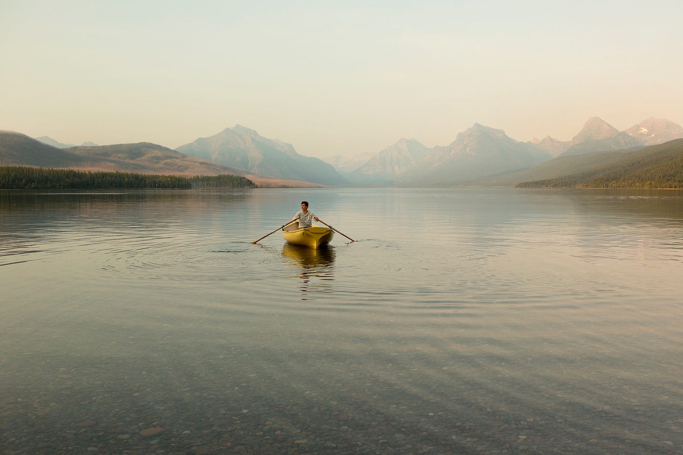 A man rowing a boat in Glacier National Park. Mood is a bit mysterious and muted.