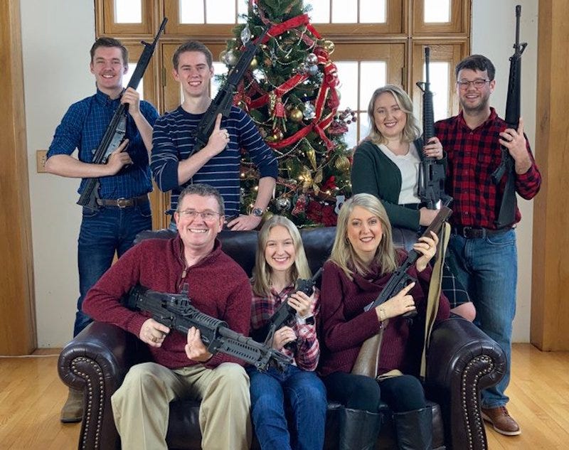 Seven family members holding assault rifles in front of Christmas tree