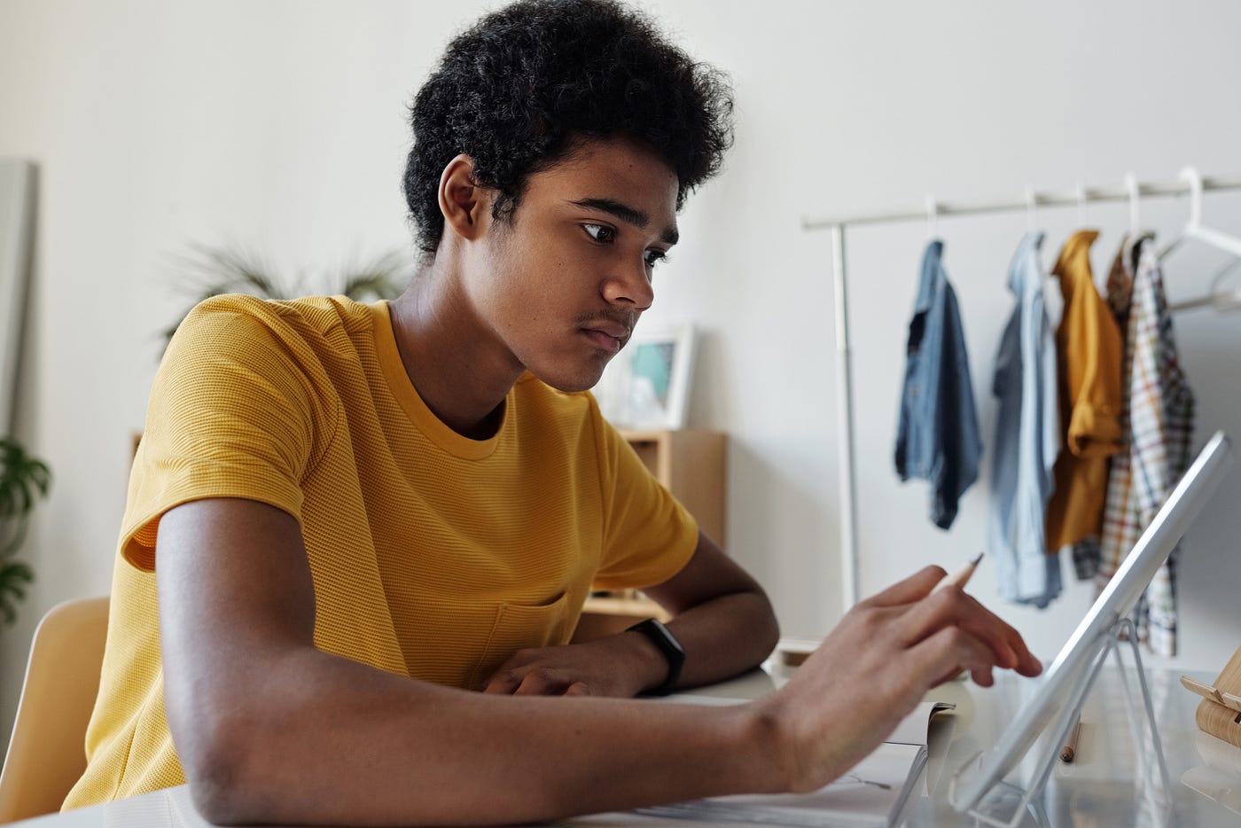 A young man in a yellow t shirt works at his desk with a cheerful look of determination on his face