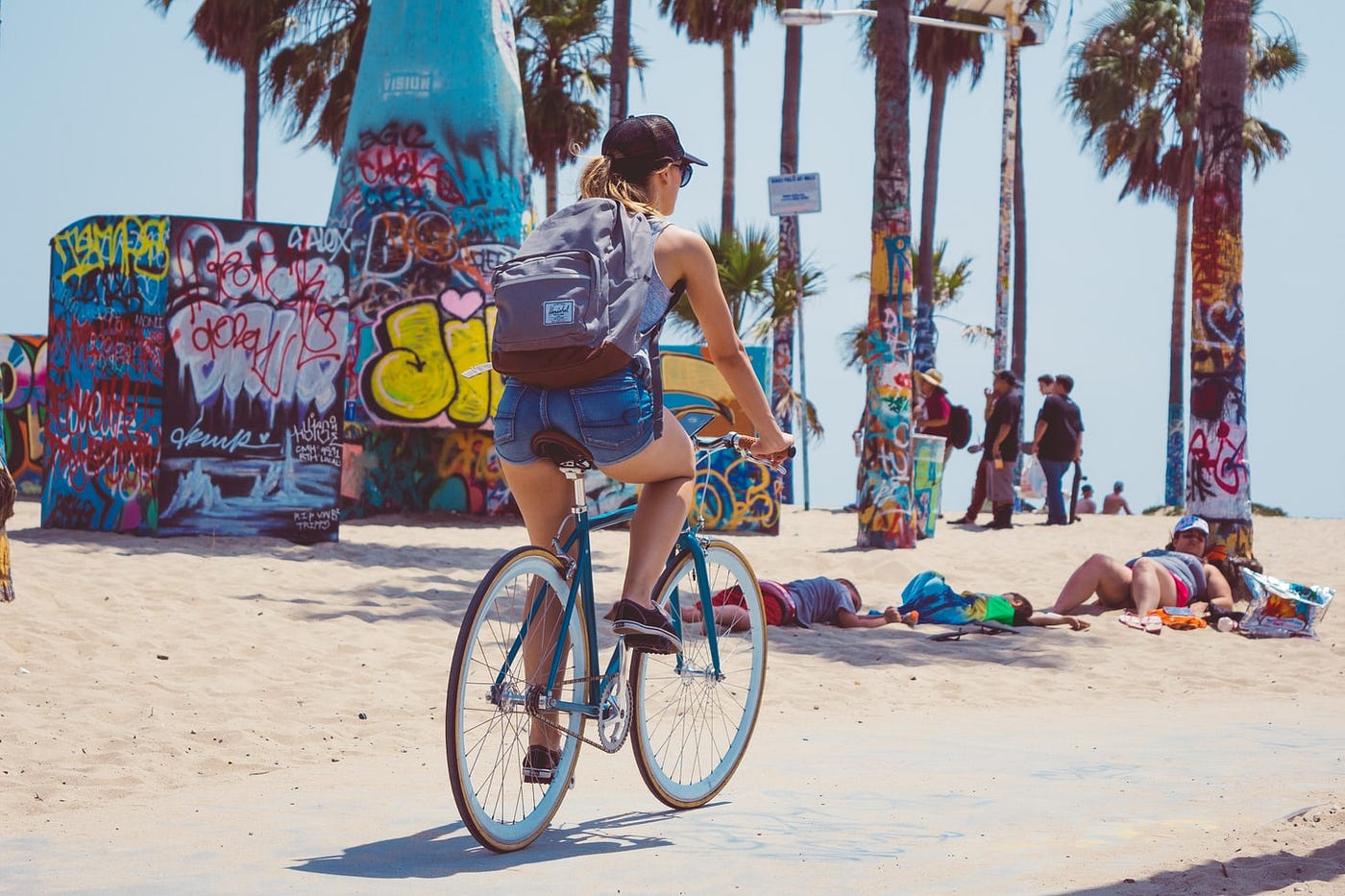 A woman bikes with a backpack along a beach walkway.
