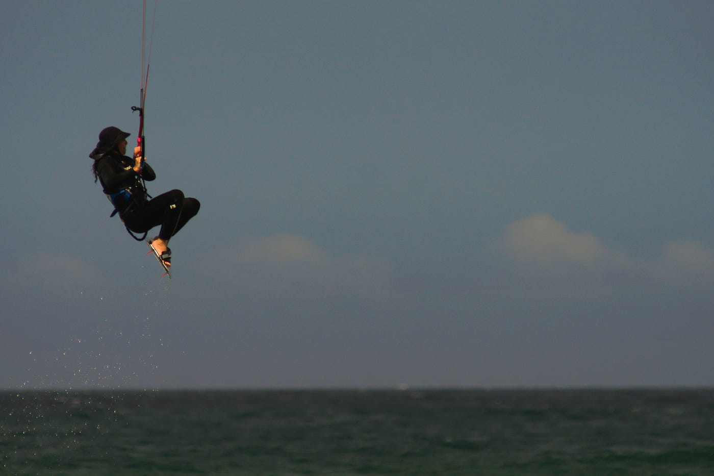 An image of Uzi windsurfing — you can’t see the parachute, just the sky, the ocean and Uzi dangling from a harness in mid-air.