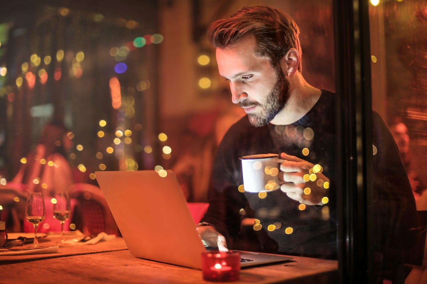 A man working on a laptop while holding a cup of coffee.