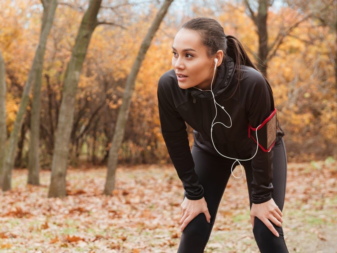 Woman wearing black exercise clothing with her hands on her knees.