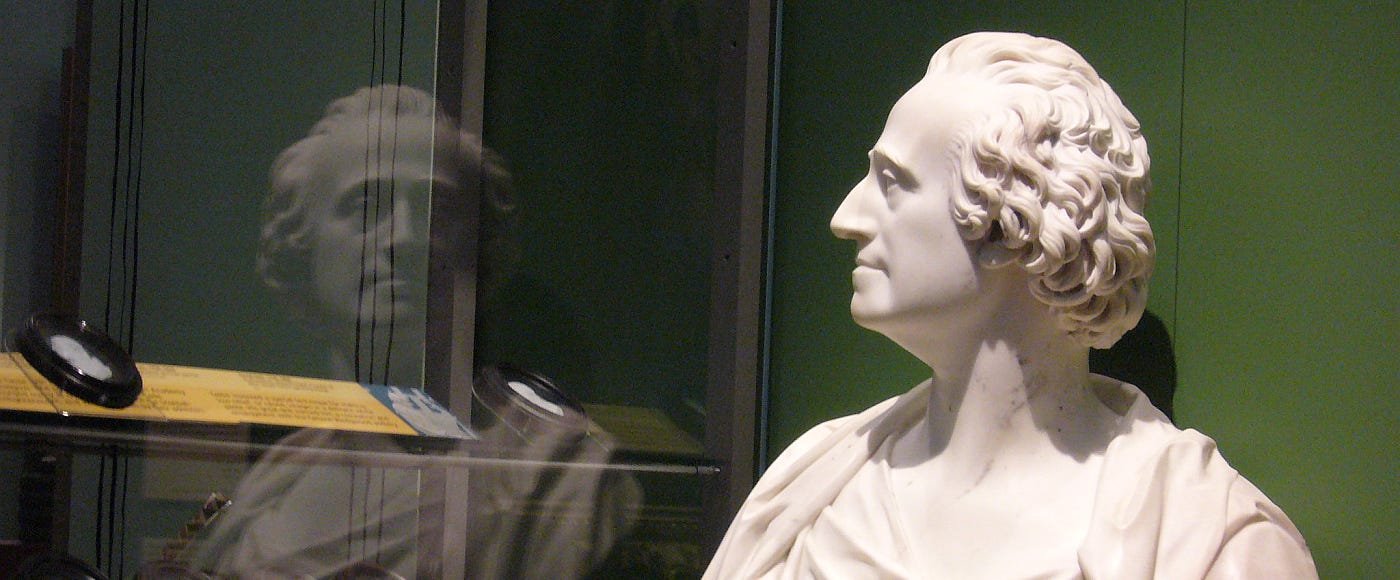 A bust of Adam Smith, reflected in a glass display cabinet