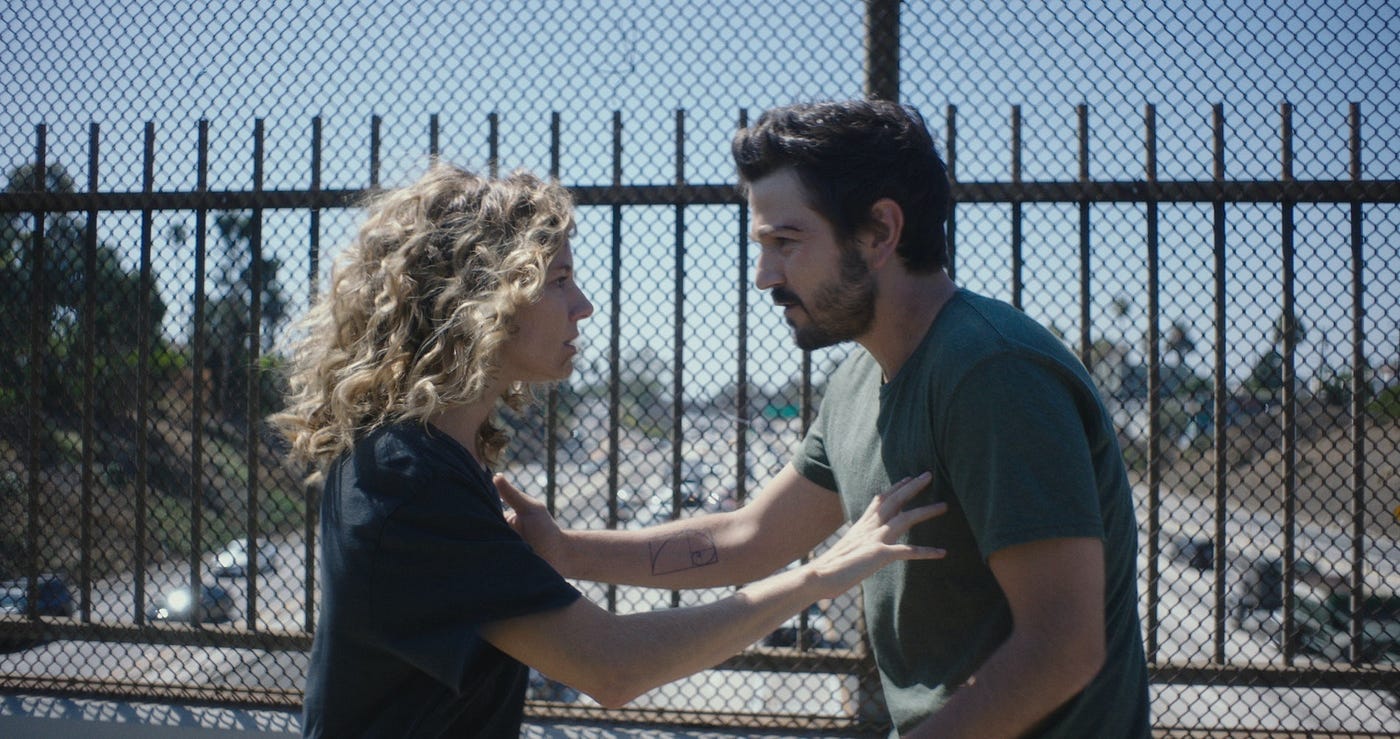 Sienna Miller and Diego Luna look at one another with intensity on a freeway overpass.