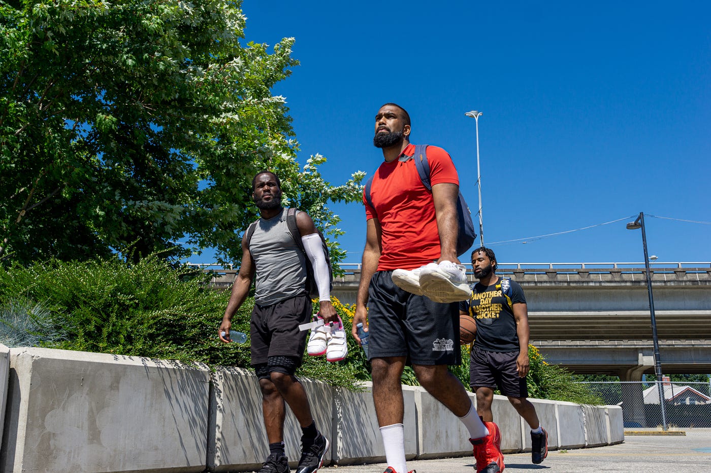 Three black men walking down the sidewalk with basketball shoes in their hands.