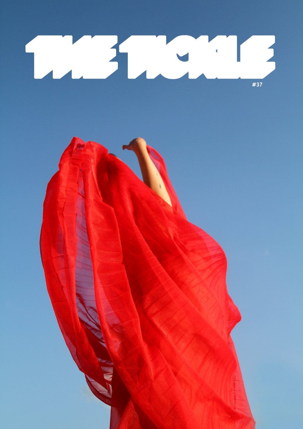 An energetic feminine figure draped in translucent red fabric, against a bright blue background. Text: “The Tickle Issue #37”