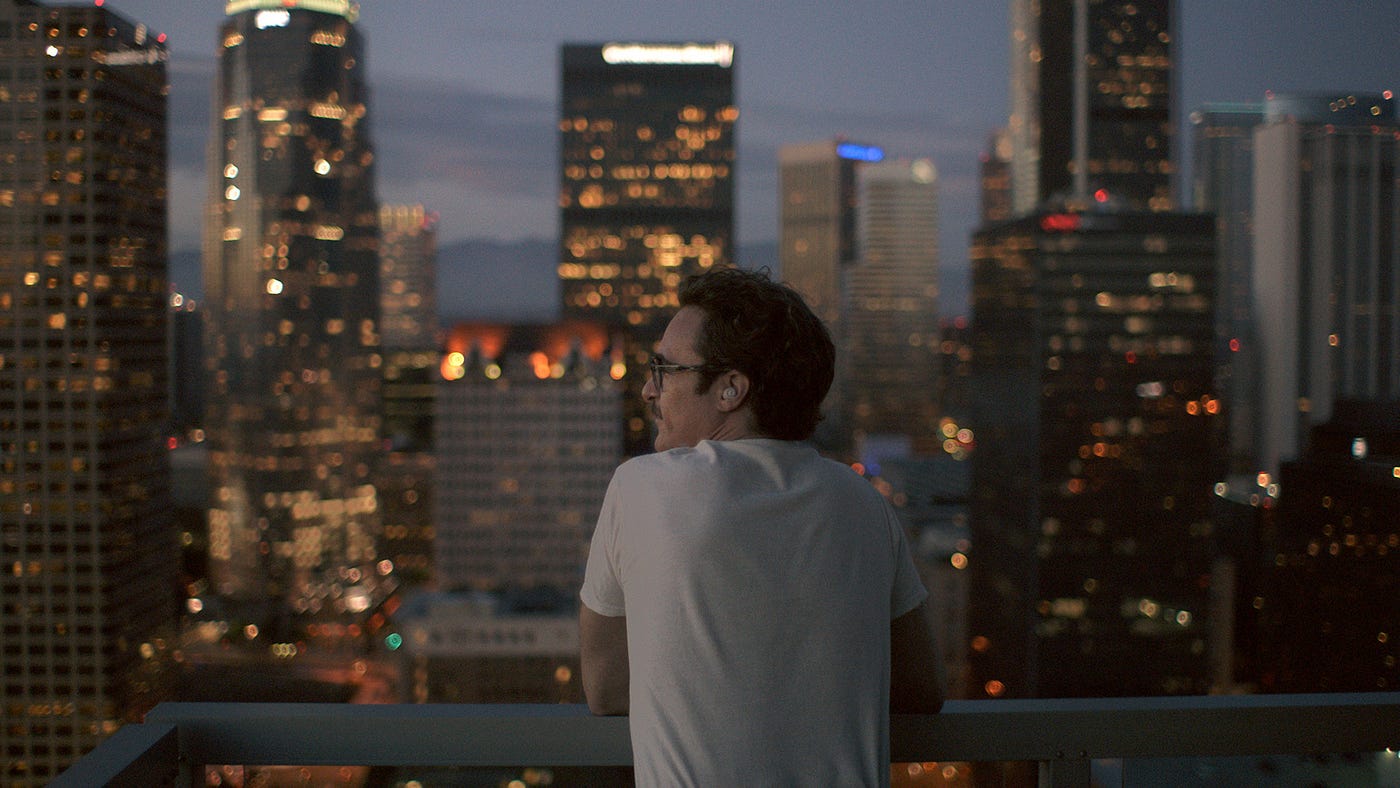 Man in white shirt overlooks city buildings and lights poignantly.