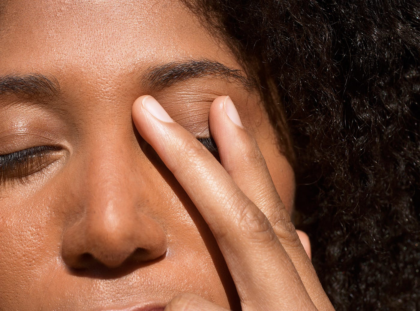 Young Black woman touching her eyelid in stress.