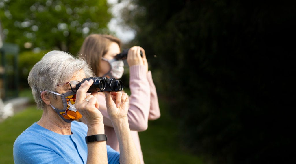 Two women wearing face masks use binoculars to look in the distance.