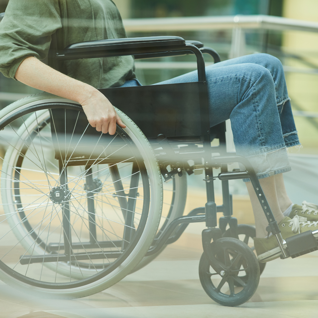 Picture of a person in a manual wheelchair. They are wearing a green shirt, blue jeans and green sneakers. Their face is not within the frame of the picture. Photo credit: Canva