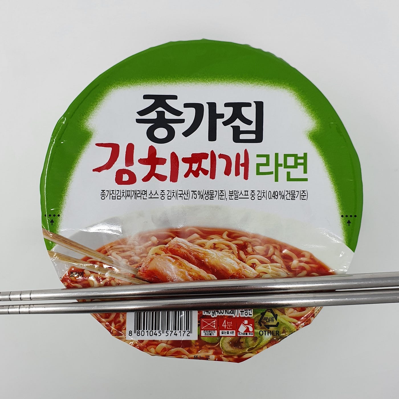 A closed cup of Jonggajip Kimchi Jjigae Ramen cooking for 4 minutes with chopsticks resting on top.