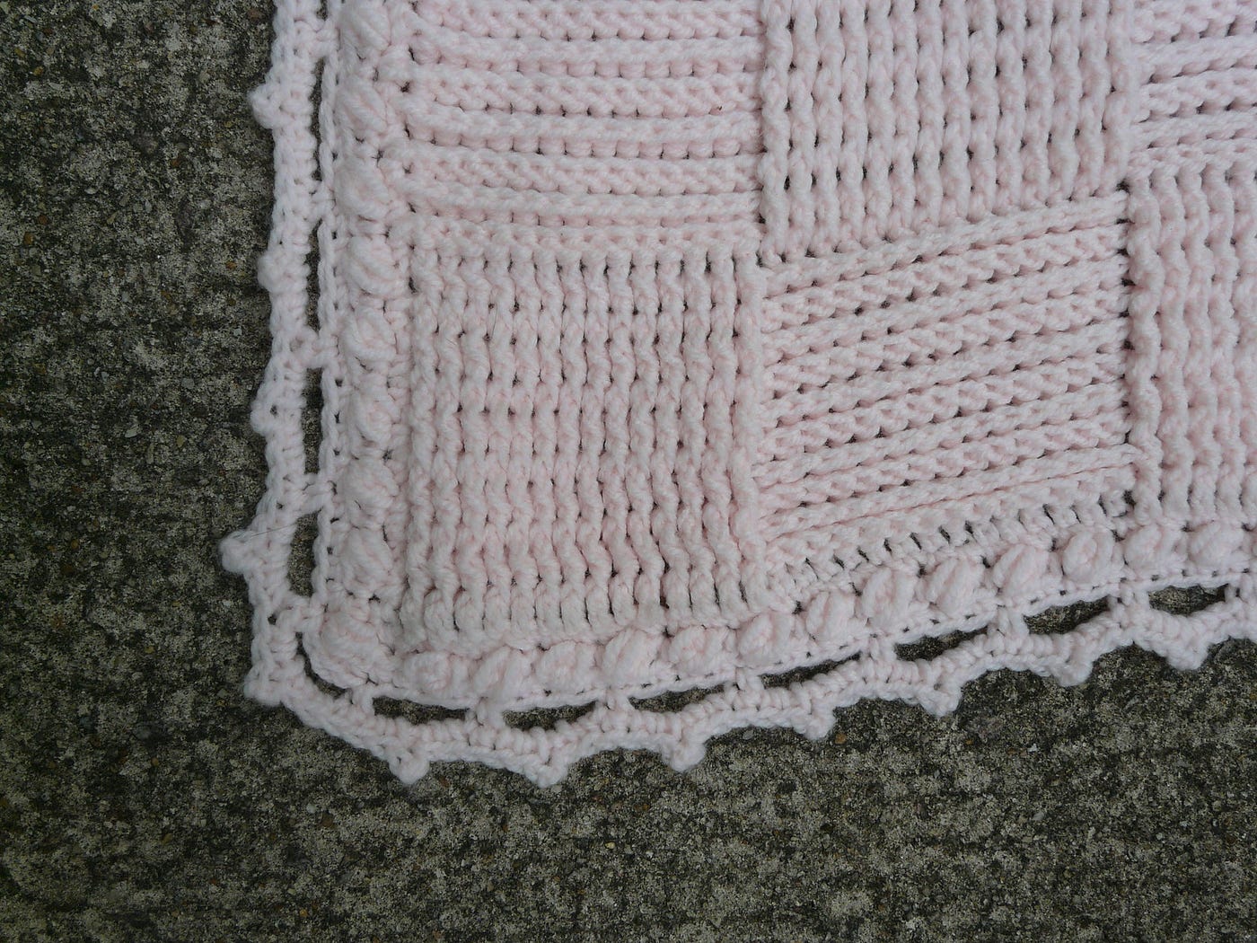 A pink crochet blanket worked in a textured basketweave stitch