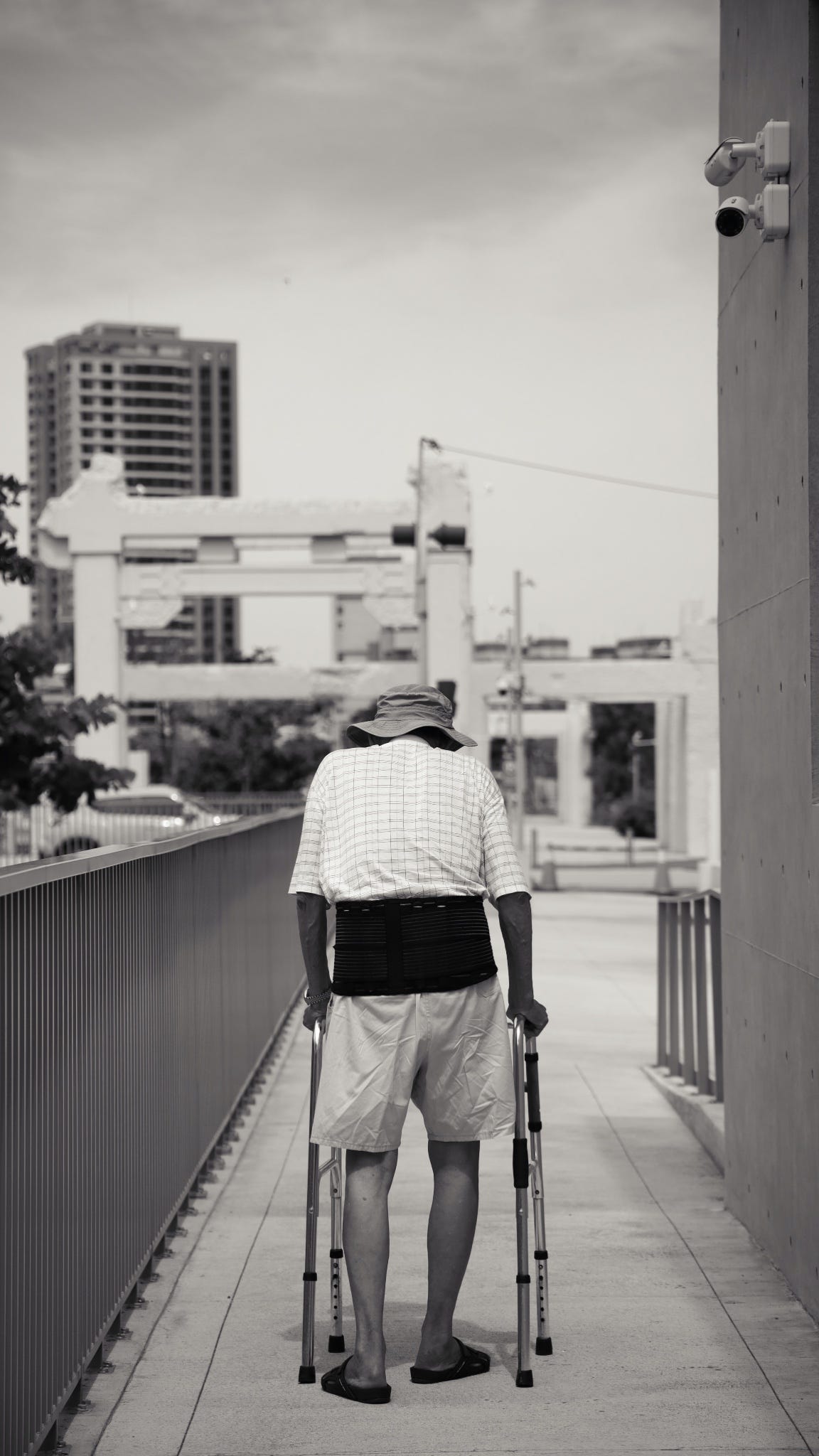 Black and white photo of a man walking with a walker outside in the summer.