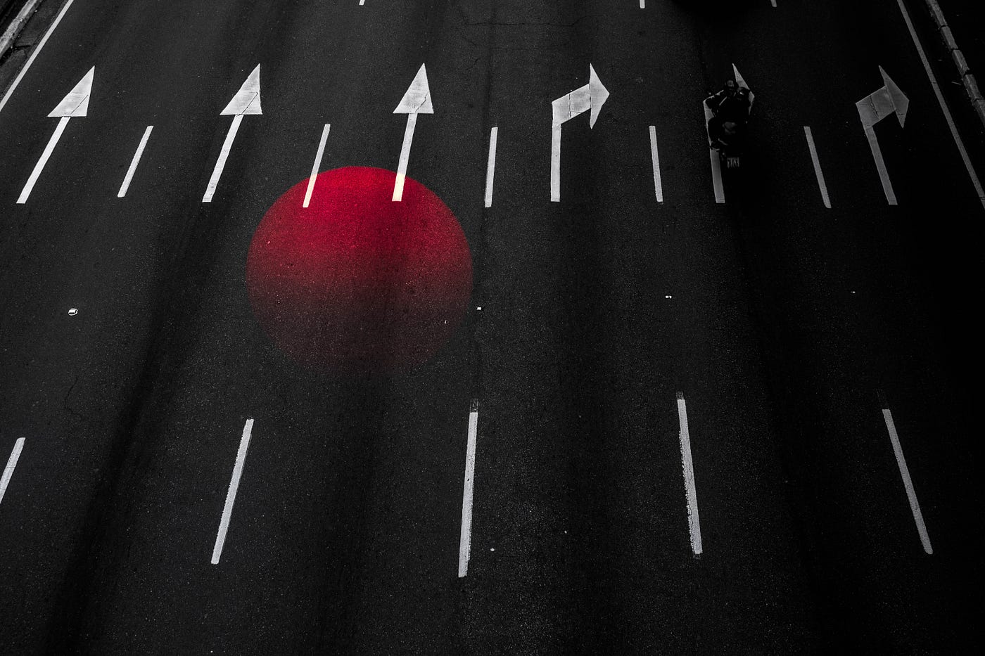 A roadway with some lanes marked with arrows pointing straight, others marking a turn, and a superimposed image of a red orb