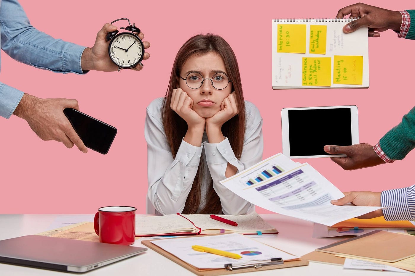 Sad female workaholic keeps hands under chin, busy making project work, studies papers, wears elegant white shirt, sits at desktop, unknown people stretch hands with notes, alarm clock.