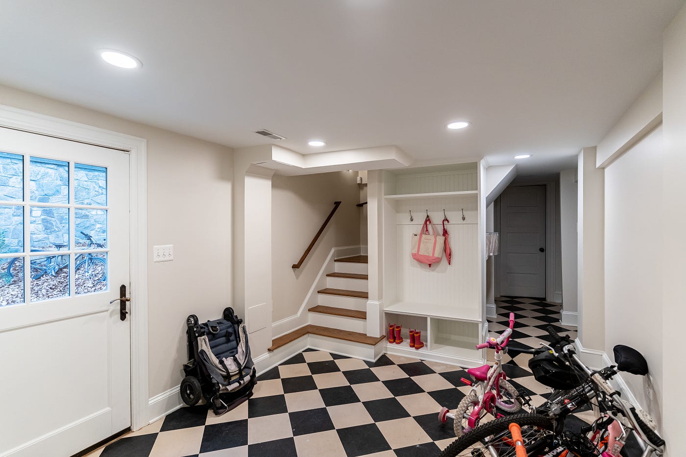 Mudroom with original checkerboard tile flooring, built in hanging and shoe storage, and bikes stored safely.