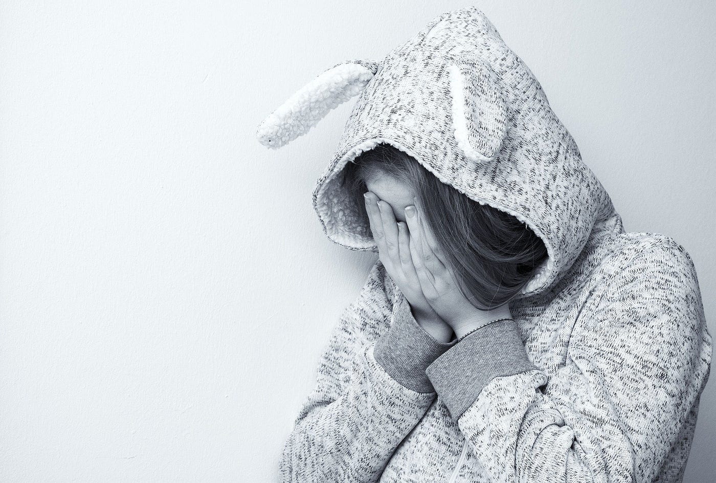 Black and white image of a young woman hiding her face wearing a hoodie with bunny ears.