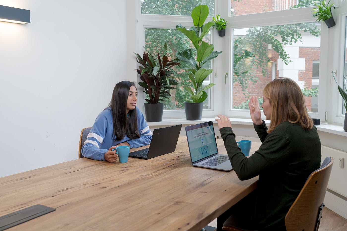 Foto entrevista con el usuario.  Dos mujeres están sentadas en una mesa con computadoras portátiles y hablando.