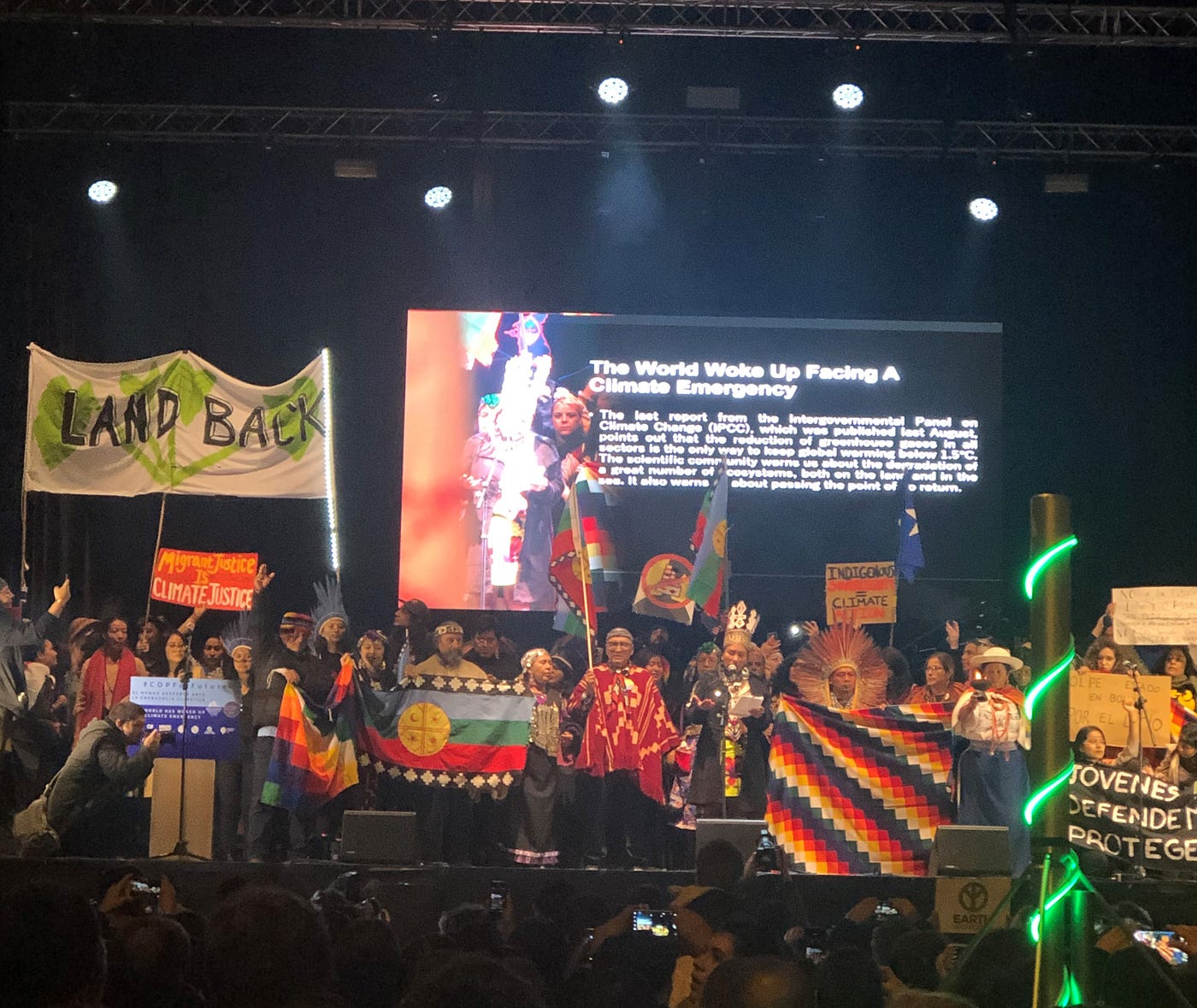 Activists stand in front of a slide presentation about climate emergency, bearing signs for Indigenous sovereignty