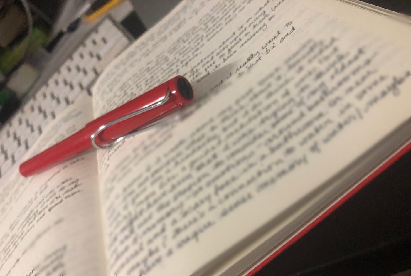 image of a journal open, with writing blurred on the page and a red fountain pen sitting on top.