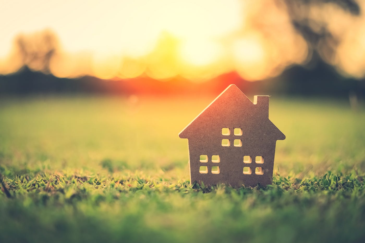 Copy space of home and life concept. Small model home on green grass with sunlight abstract background.