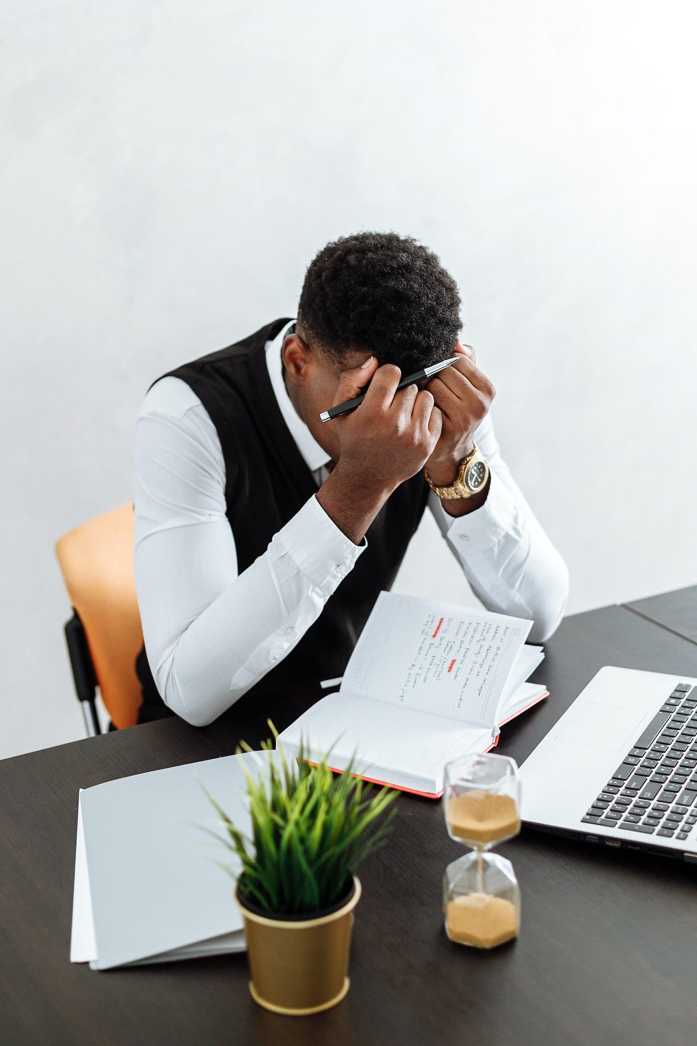 A young writer wearing an official cloth bows in his hands with regrets. He has a writing note, a desk, and laptop in front of him.