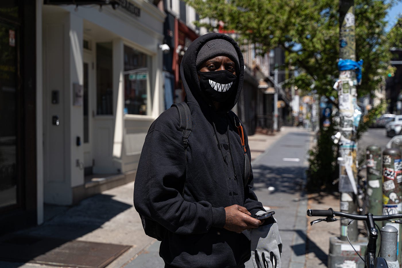 A black man poses for the photo wearing a dark hoodie, black face mask, beanie.
