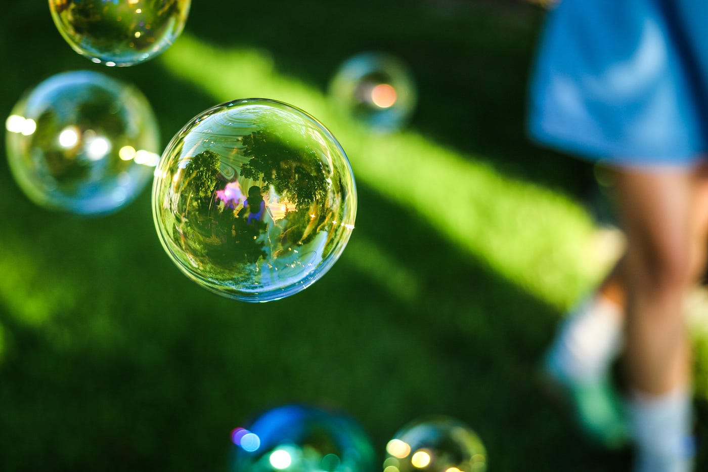 Bubbles floating in the air over green grass, with a person’s legs in the background