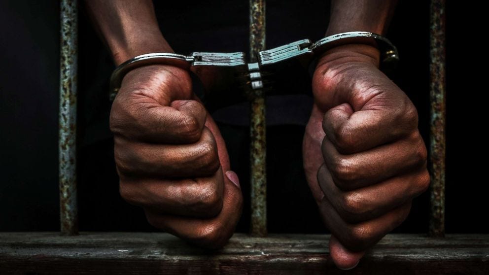 Image of African-American hands in handcuffs behind jail bars.