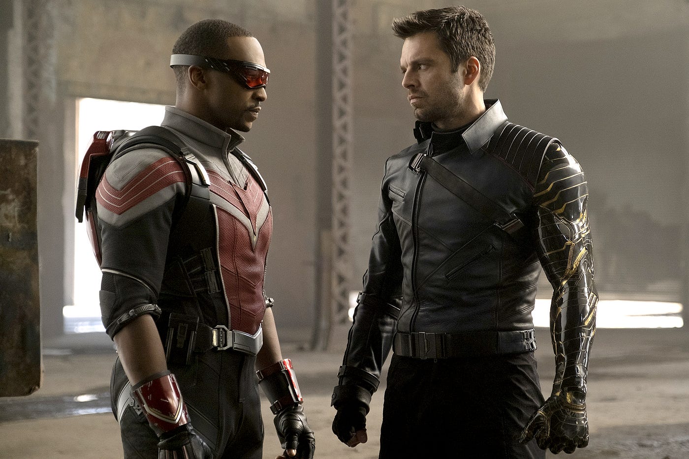 Falcon (Sebastian Stan) standing next to Winter Soldier (Anthony Mackie) in an open industrial warehouse-like space.