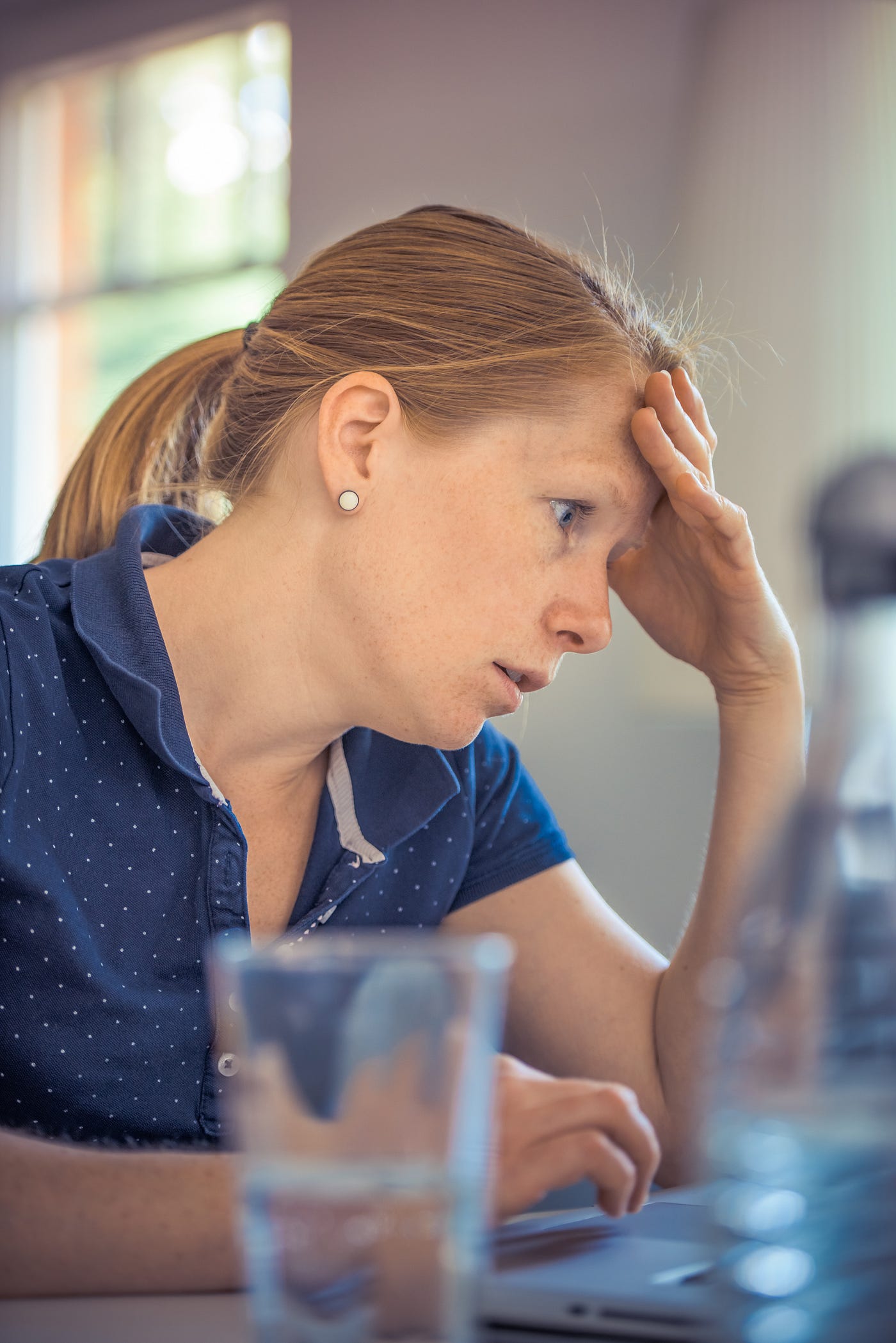 Red-headed woman with hand on head looking at computer