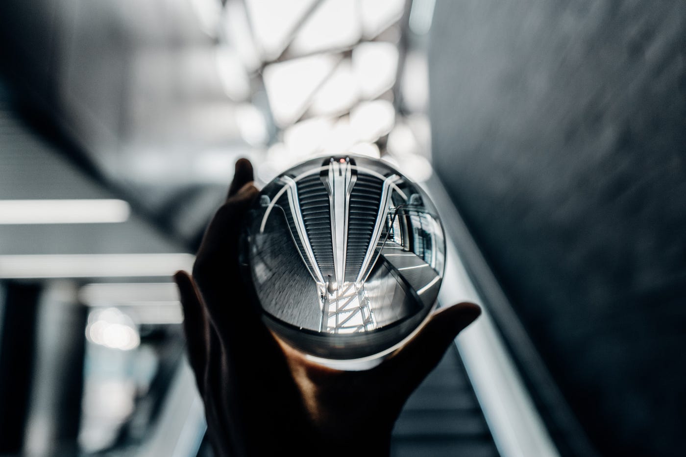 Hands holding a glass orb. You can see the reflection of a set of escalators in the glass orb.