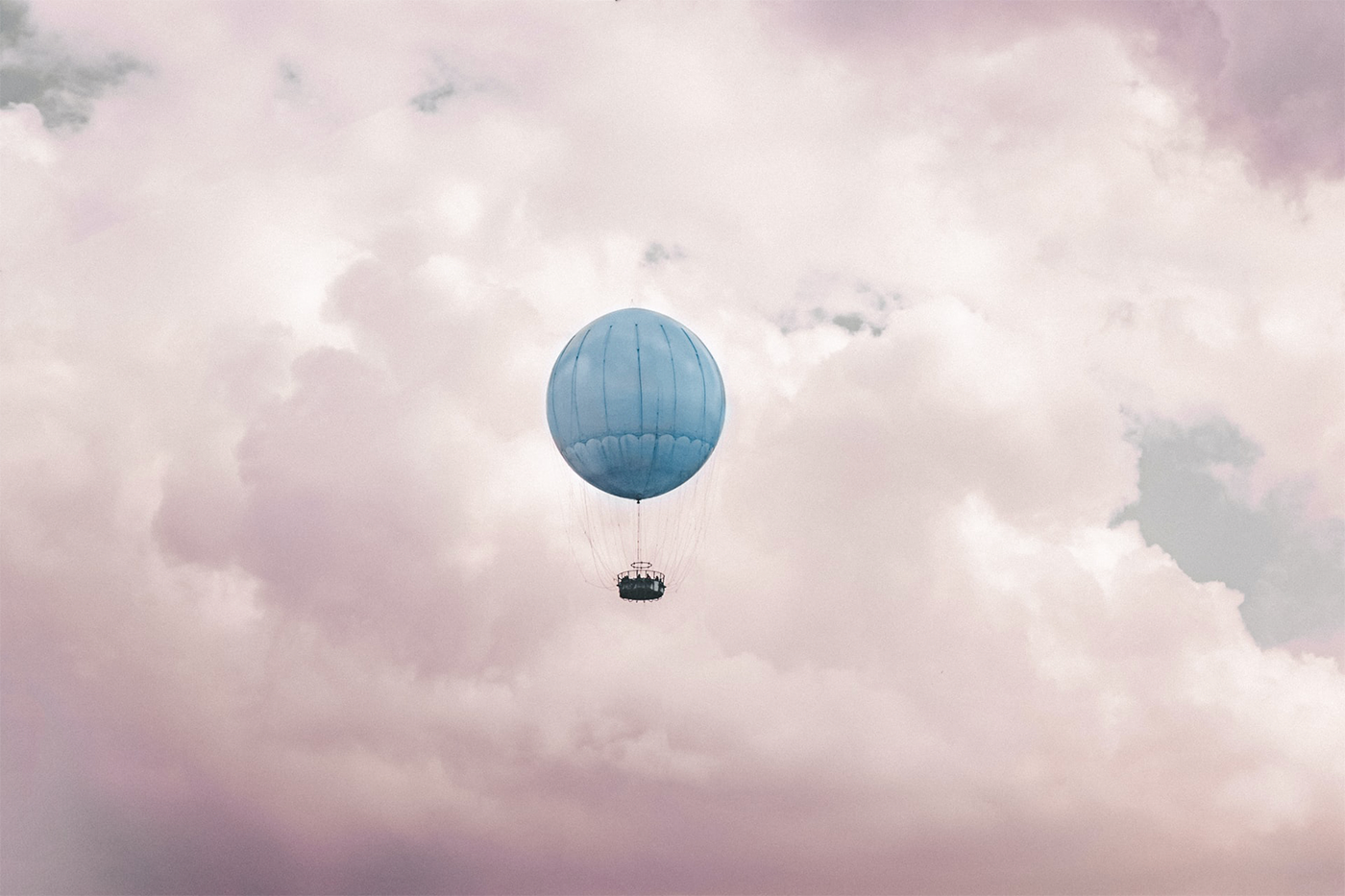A hot air balloon floating through pink and pastel clouds.