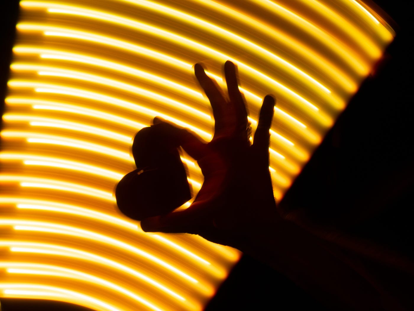 Hand holding a heart in front of a bright yellow virtual background.